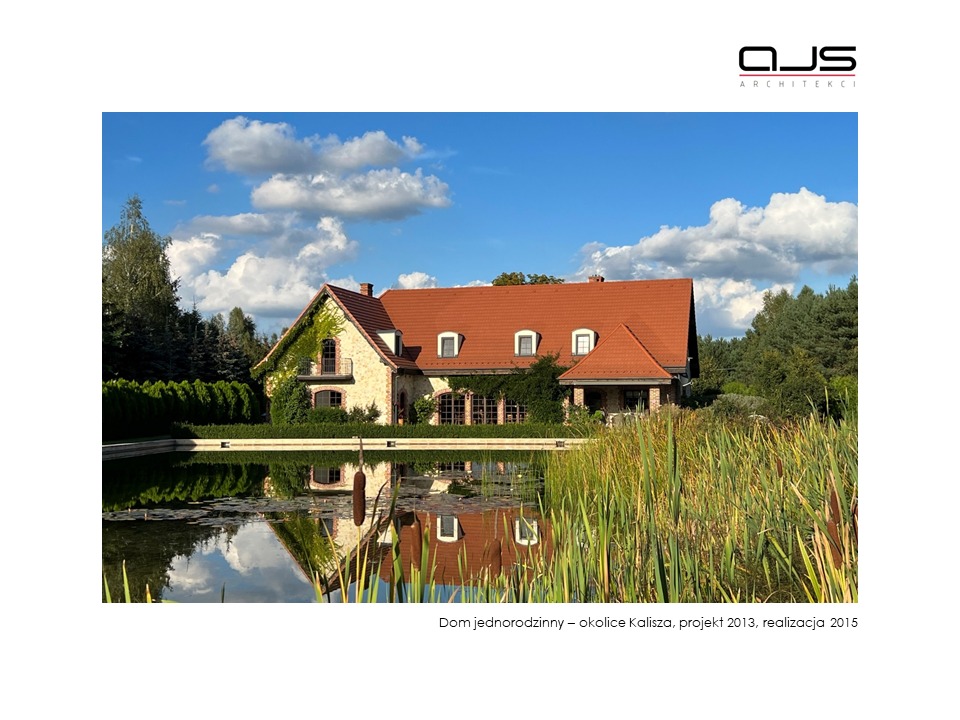 Dom jednorodzinny z czerwoną dachówką, otoczony zielenią i stawem, którego tafla odbija budynek i błękitne niebo z chmurami. Logo architektoniczne w prawym górnym rogu.