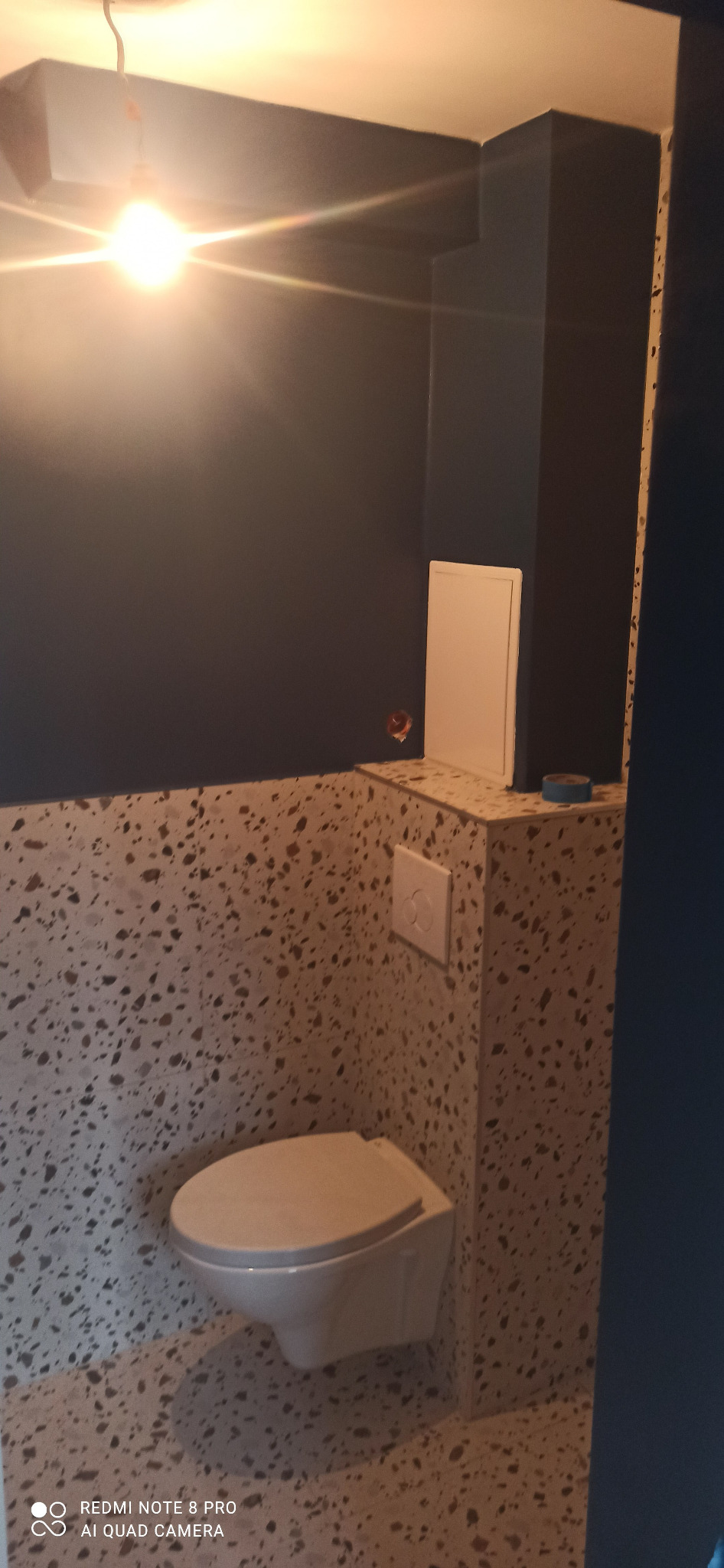 Nowoczesna toaleta podwieszana z mozaikową okładziną ścian i ciemnoniebieską ścianą, widoczna instalacja elektryczna.