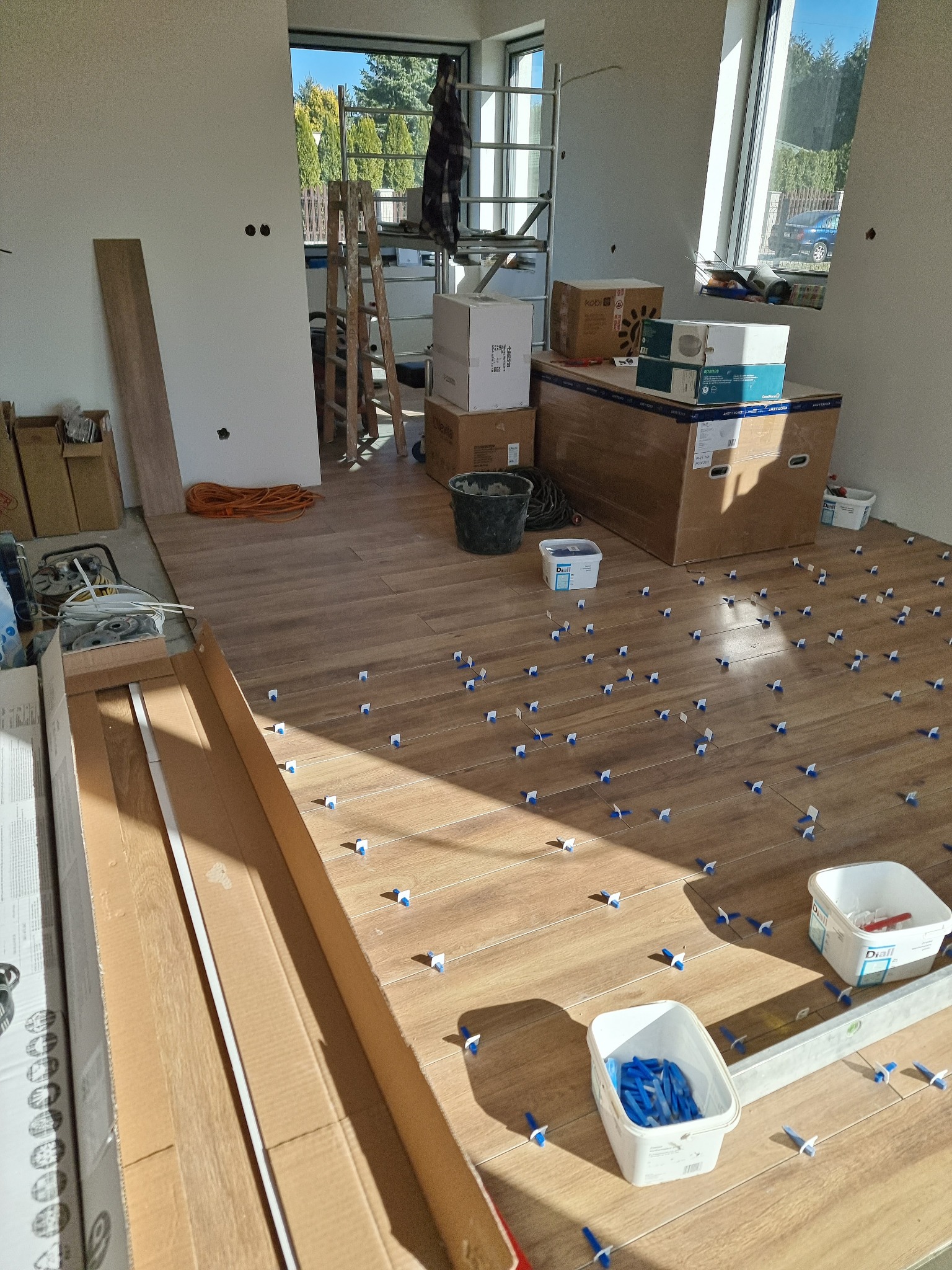 Układanie drewnopodobnych płytek podłogowych z użyciem klipsów poziomujących w trakcie remontu w Łodzi, widoczne narzędzia i materiały budowlane.