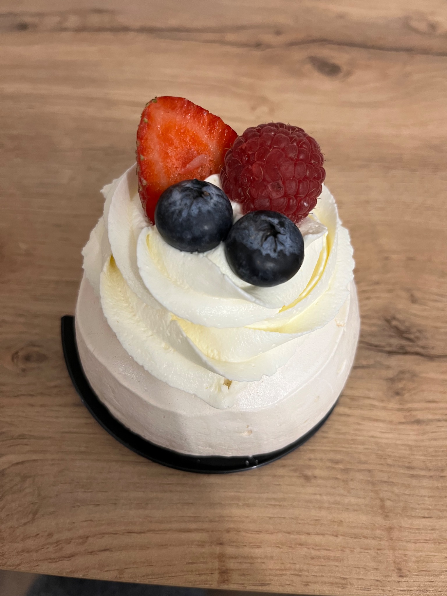 Mini deser z kremem, truskawką, maliną i borówkami na drewnianym stole.