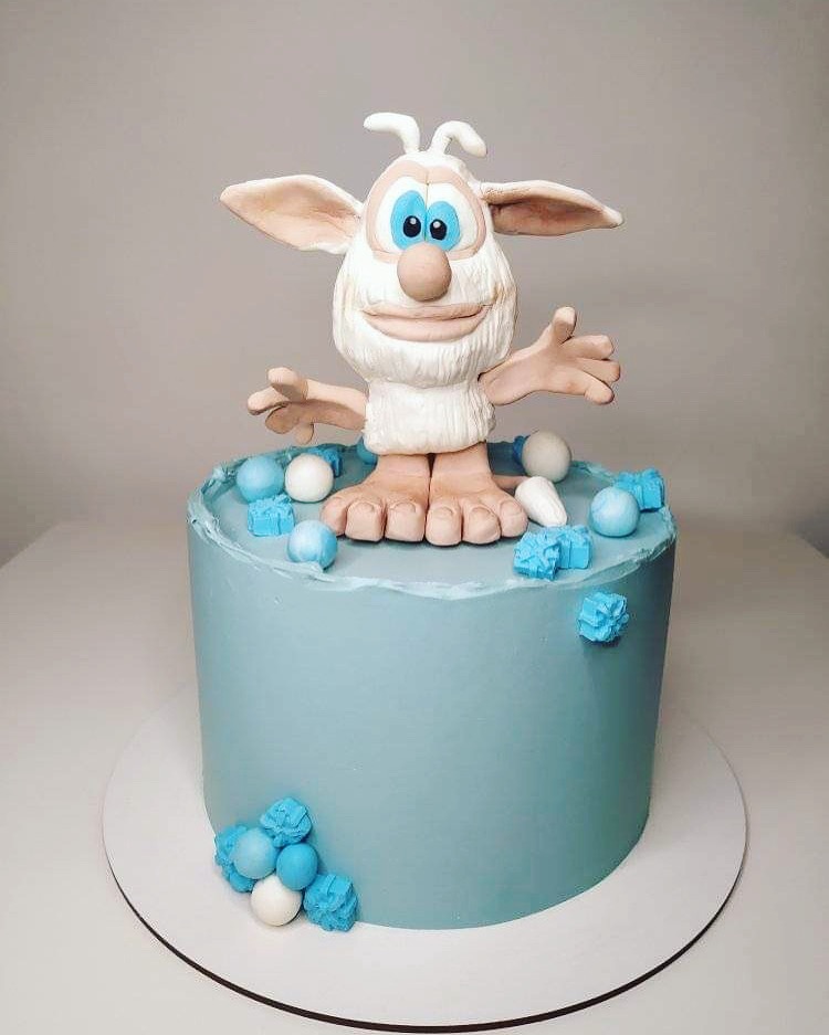 Tort w odcieniach błękitu z figurką bajkowej postaci Booba i dekoracjami z kulek i kostek lukru.