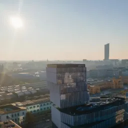 Widok z góry na nowoczesny budynek biurowy z logo Oferteo, w tle panorama miasta w porannym słońcu i mglistej atmosferze.