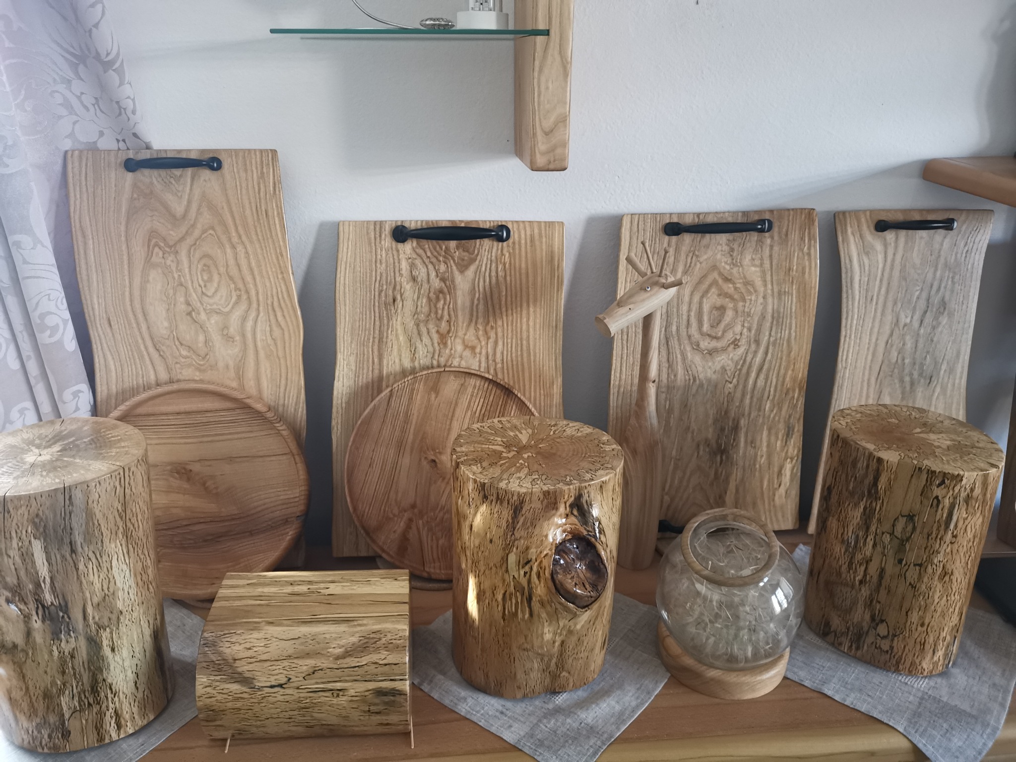 Drewniane deski do krojenia z uchwytami, okrągłe tace i pniaki z widocznymi słojami drewna, ustawione na drewnianym blacie z szarą serwetą.