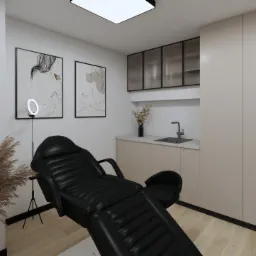 Wnętrze gabinetu z czarnym fotelem kosmetycznym, lampą pierścieniową, dekoracjami z suszonych traw, umywalką i minimalistycznymi obrazami na ścianie.