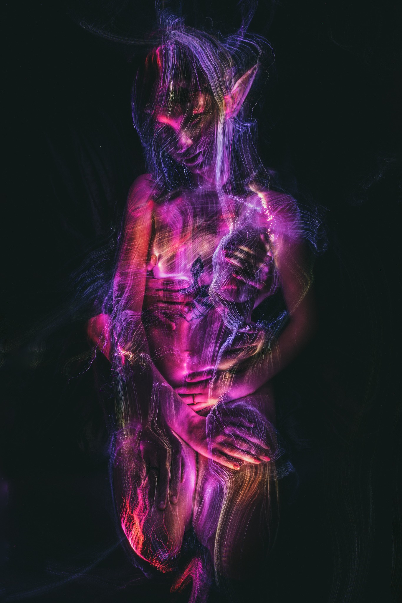 Artystyczne ujęcie nagiej kobiety z elfimi uszami, otulonej w wiązki fioletowo-różowego światła na czarnym tle.