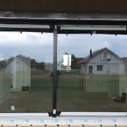 Duże, dwuczęściowe okno z czarną ramą i zamontowaną roletą zewnętrzną w surowym stanie budynku, widoczne oznaczenia VEKA na dolnej ramie okna.