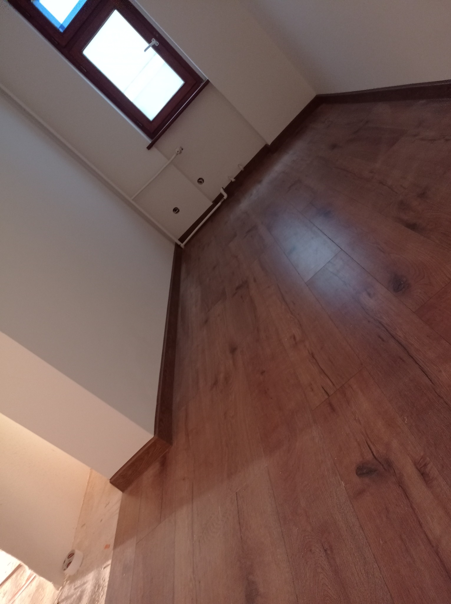 Ukończone układanie paneli podłogowych w pokoju z oknem dachowym, widoczne listwy przypodłogowe