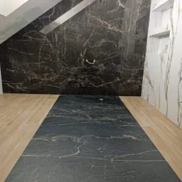 Łazienka w trakcie prac wykończeniowych, z ciemną marmurową okładziną ścienną i podłogą, kontrastującą z jasnymi panelami podłogowymi po bokach.