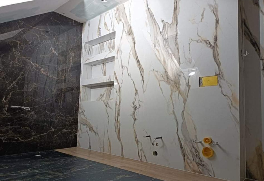 Wykończona łazienka z marmurowymi płytkami w odcieniach bieli i brązu, z wnękami w ścianie i widocznymi instalacjami hydraulicznymi przed montażem armatury.