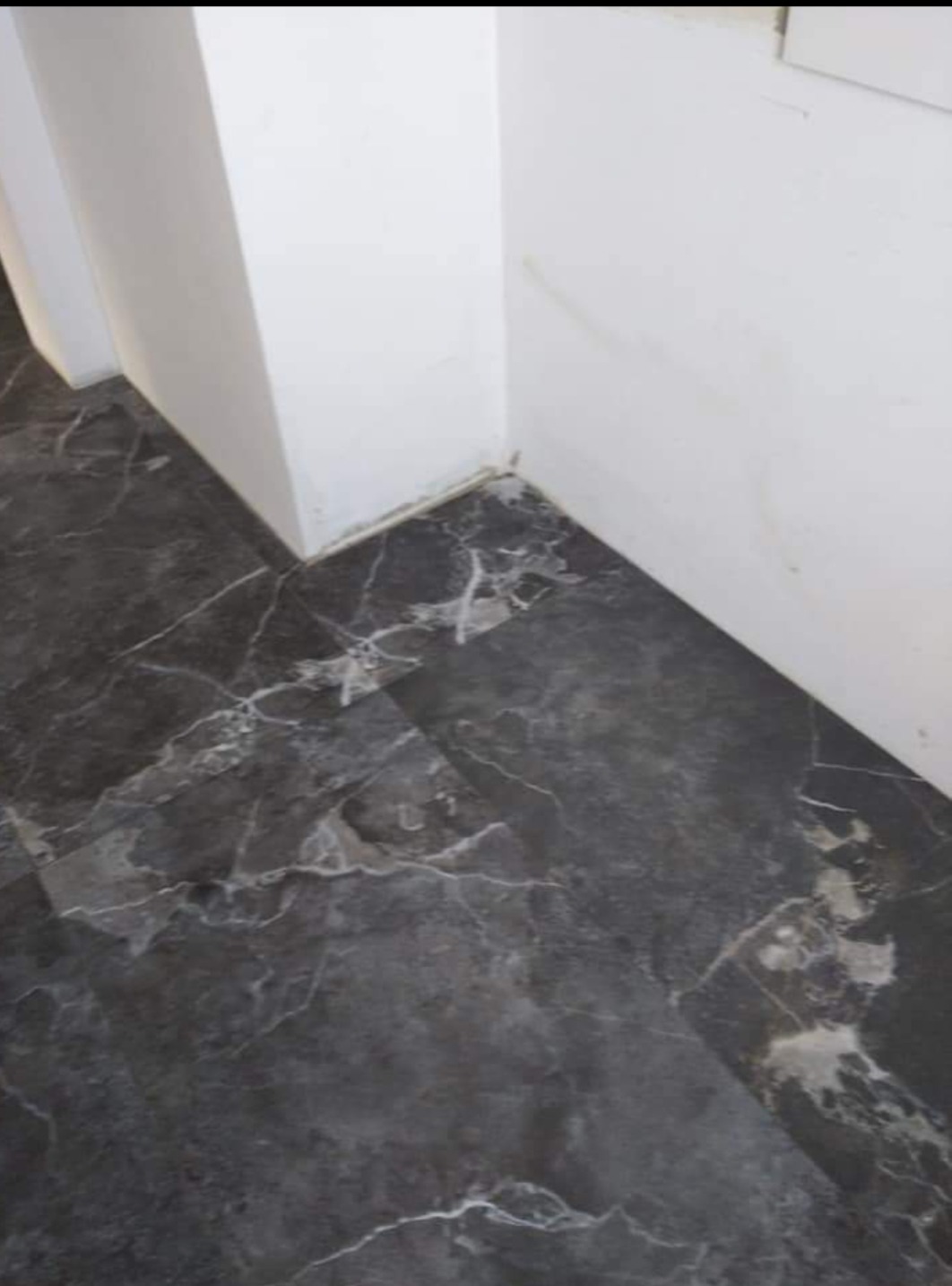 Ułożone ciemnoszare panele podłogowe imitujące marmur, widoczne przy białej ścianie w rogu pomieszczenia.