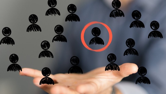 Dłoń prezentuje graficzne sylwetki ludzi, jedna z nich zaznaczona czerwonym okręgiem, symbolizująca wybór kandydata.