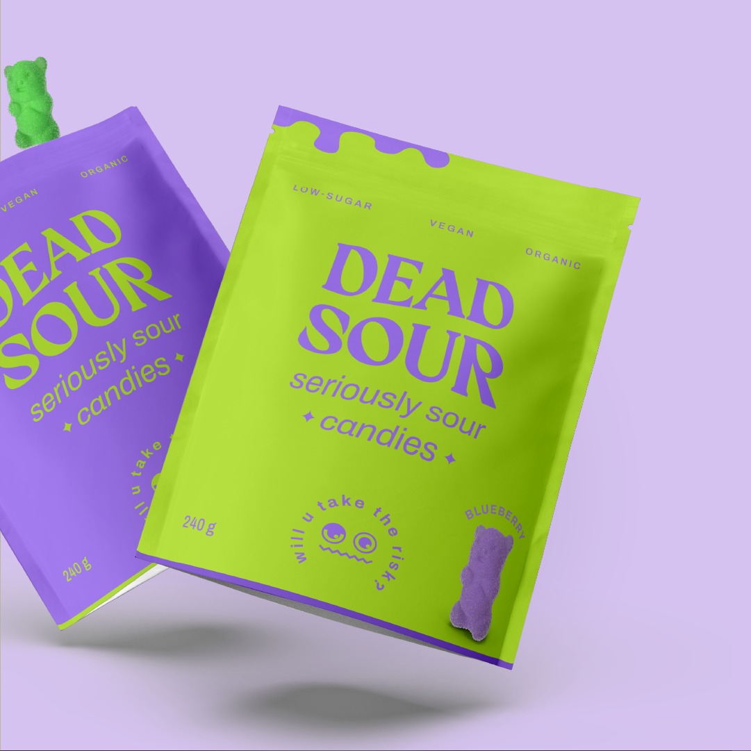 Dwa opakowania cukierków Dead Sour: jedno fioletowe z zielonym żelkiem na górze, drugie limonkowo-zielone z fioletowym żelkiem u dołu. Opakowania z napisem 'Dead Sour seriously sour candies'...