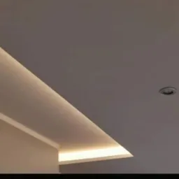 Nowoczesny sufit z oświetleniem LED wzdłuż krawędzi, okrągły punkt świetlny w górnym rogu.