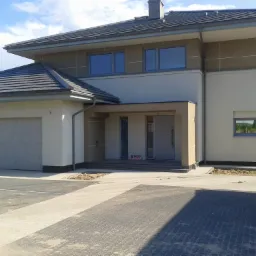 Nowoczesny dom jednorodzinny z szarymi oknami i garażem, widok z zewnątrz, częściowo wykończony teren wokół.