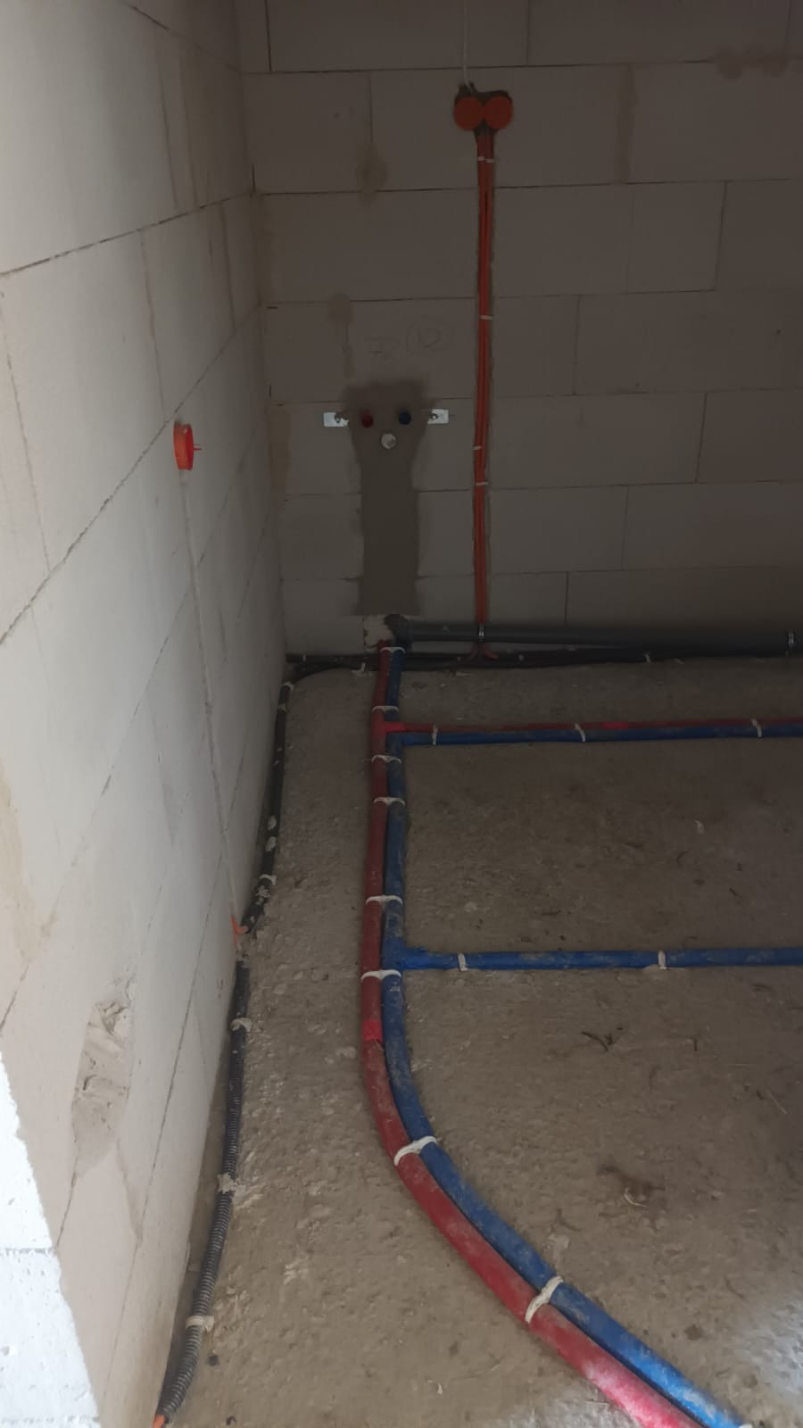 Surowy stan: Instalacja rur wodnych (czerwone i niebieskie) oraz rur osłonowych w ścianie z betonu komórkowego podczas budowy domu.