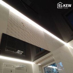 EL-KEW - Nowoczesna łazienka z białymi i czarnymi płytkami, oświetleniem LED i czarnym sufitem podwieszanym, widoczne logo firmy EL-KEW Elewacje w prawym górnym rogu.