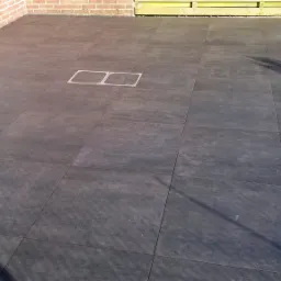 Wyłożony grafitowymi płytkami taras z odpływem liniowym przy krawędzi, widoczna ceglana ściana i właz rewizyjny na środku