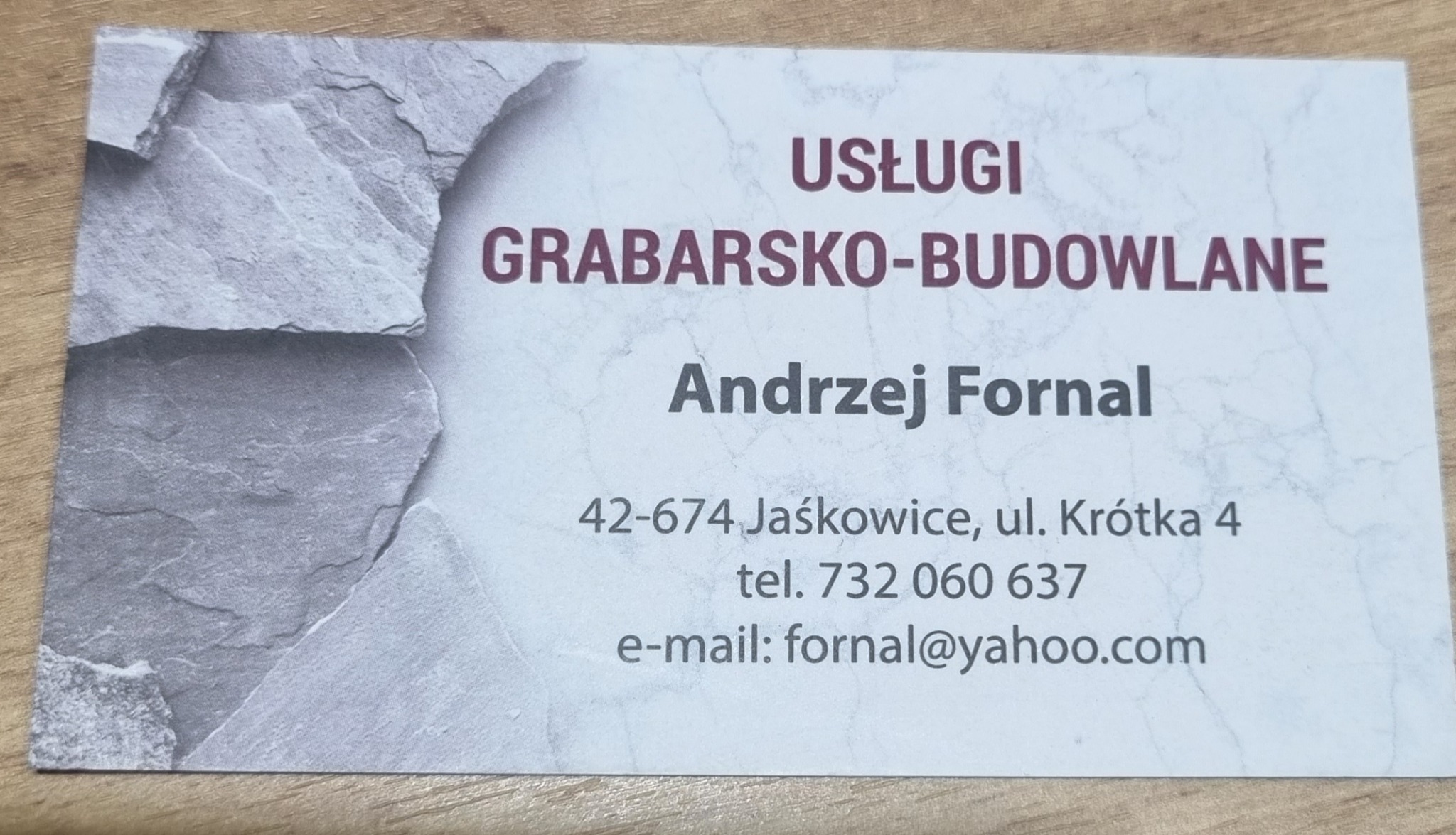 Wizytówka firmy świadczącej usługi grabarsko-budowlane, z adresem, numerem telefonu i adresem e-mail, na tle imitującym strukturę kamienia.