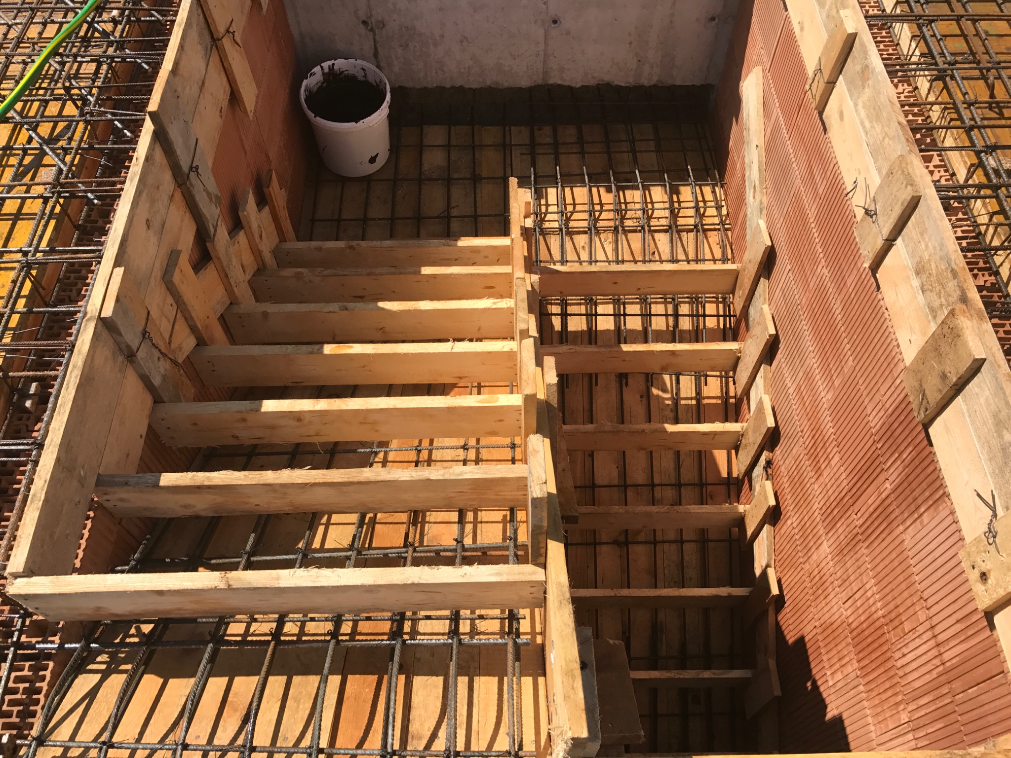 Szalunek drewniany zbrojony stalą pod wylewkę fundamentów z widocznym kubełkiem z zaprawą w rogu.