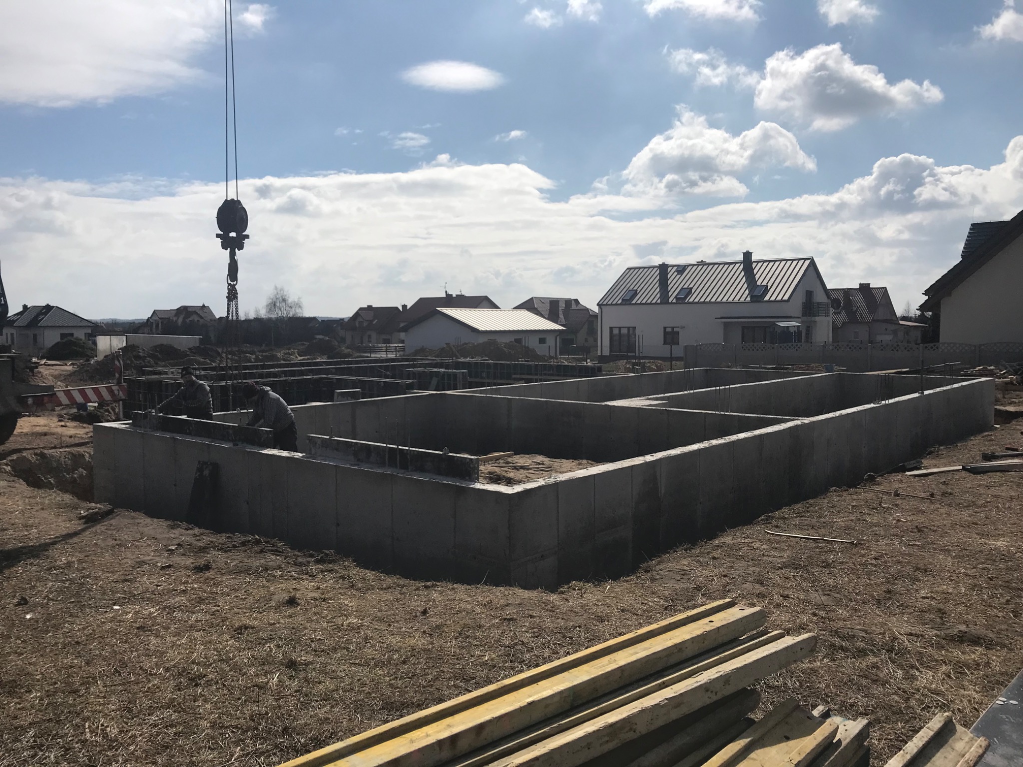 Wylane fundamenty pod budowę domu jednorodzinnego w Morawicy, widoczne zbrojenia i szalunki, w tle zabudowa mieszkalna i dźwig budowlany.