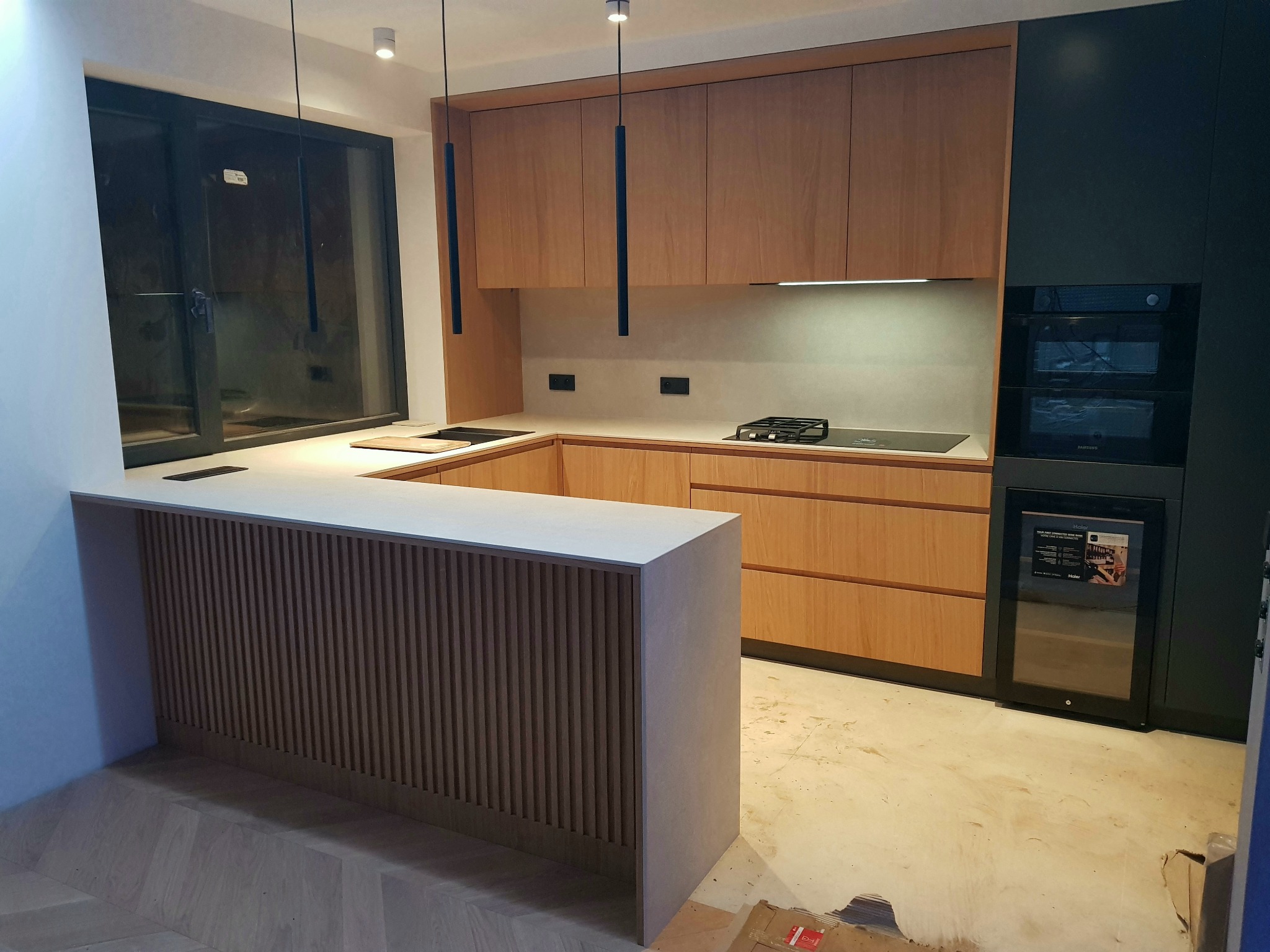 Nowoczesna kuchnia z drewnianymi frontami w odcieniach brązu i czarnymi elementami zabudowy, widziana z perspektywy wyspy kuchennej z ryflowanym wykończeniem w Oświęcimiu.