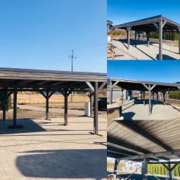 Drewniana wiata garażowa z płaskim dachem, pomalowana na ciemny kolor, na jasnej kostce brukowej w słoneczny dzień. Widoczne podpory z drewna i konstrukcja dachu od spodu.