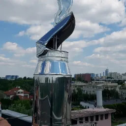 Błyszczący, metalowy wkład kominowy z deflektorem, zamontowany na kominie z widokiem na miejski krajobraz w oddali.