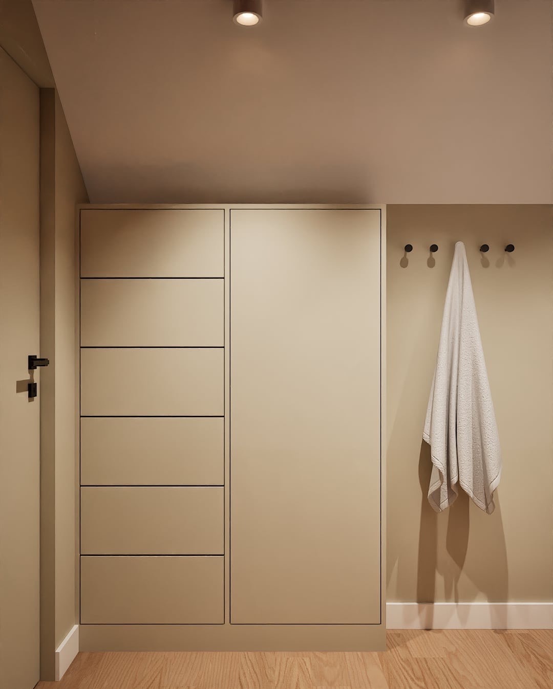 Beżowa szafa z szufladami i wieszakami na ręcznik w minimalistycznym wnętrzu, oświetlonym punktowymi lampami sufitowymi i drewnianą podłogą.