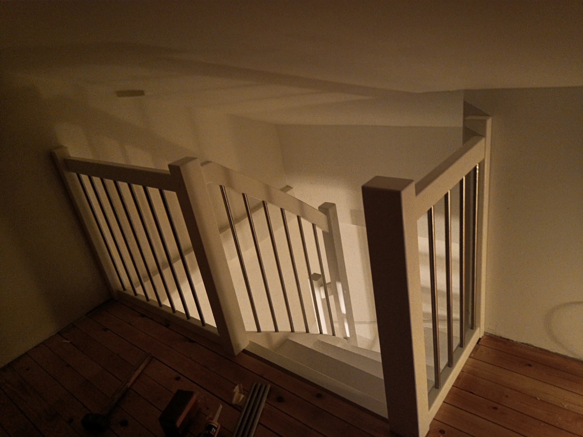 Widok z góry na białe schody z metalowymi balustradami, drewniana podłoga, narzędzia w rogu