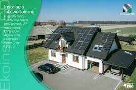 Dom z zainstalowanymi panelami słonecznymi na dachu, widoczny samochód osobowy na podjeździe, reklama instalacji z boku zdjęcia.