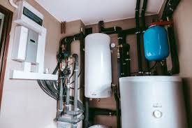 Wnętrze kotłowni z białym zbiornikiem akumulacyjnym ciepła, niebieskim naczyniem przeponowym oraz rozbudowaną instalacją rurową i elektryczną.