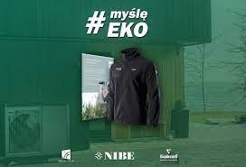 Zdjęcie promocyjne z kurtką na tle zielonej ściany z hasłem #myślę #EKO, widoczna pompa ciepła NIBE i logo Soltherm.
