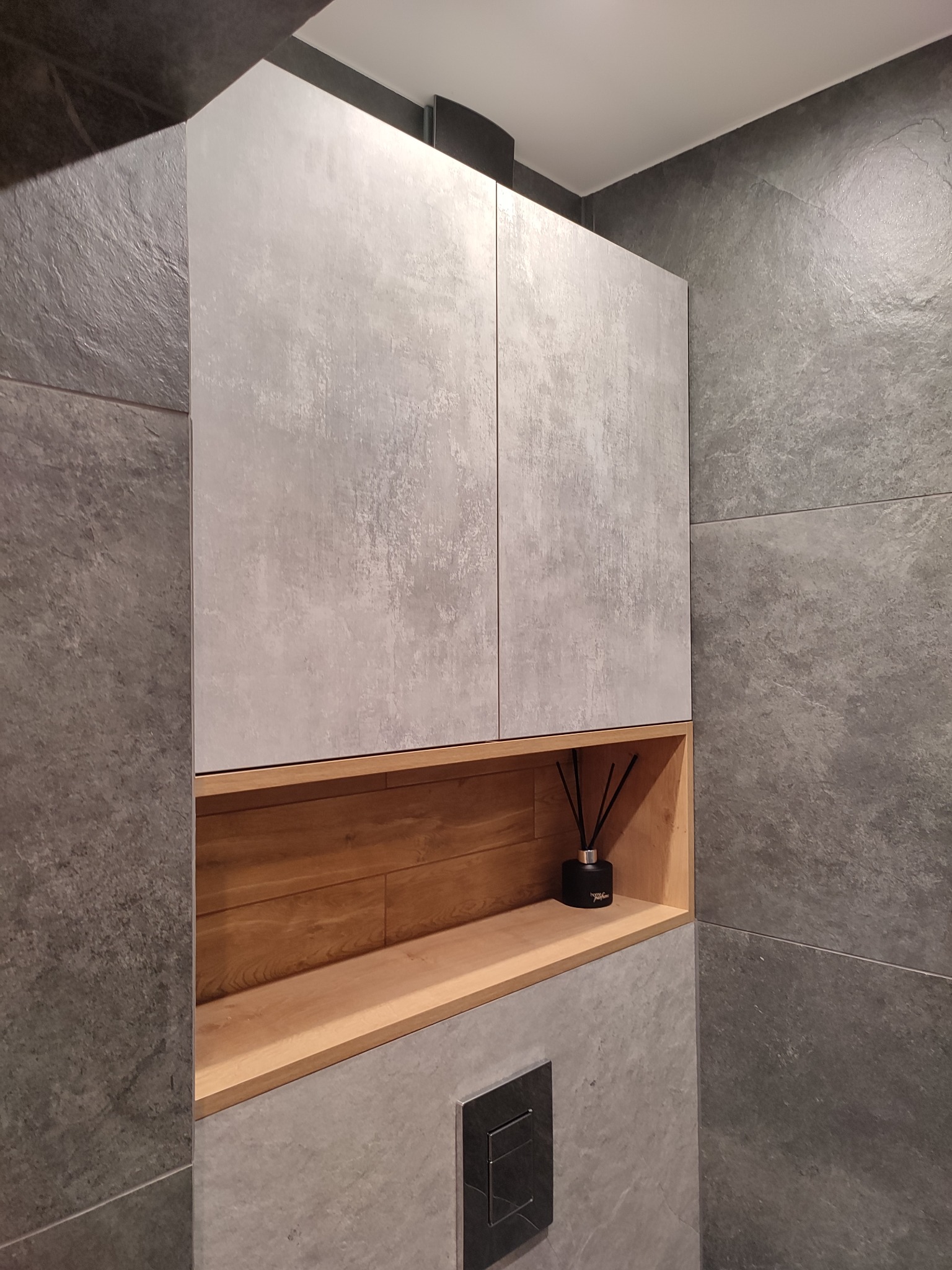 Szafka łazienkowa na wymiar z drewnianą wnęką i dyfuzorem zapachowym, wykonana w Zielonej Górze, wkomponowana w szarą, nowoczesną łazienkę.