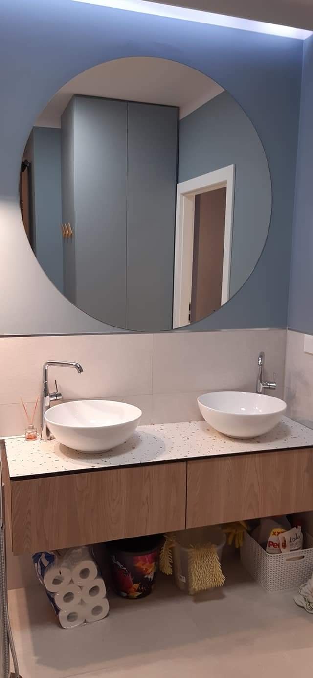 Łazienka z dwoma umywalkami nablatowymi, drewnianą szafką pod umywalką i okrągłym lustrem, w którym odbija się szafa i drzwi.