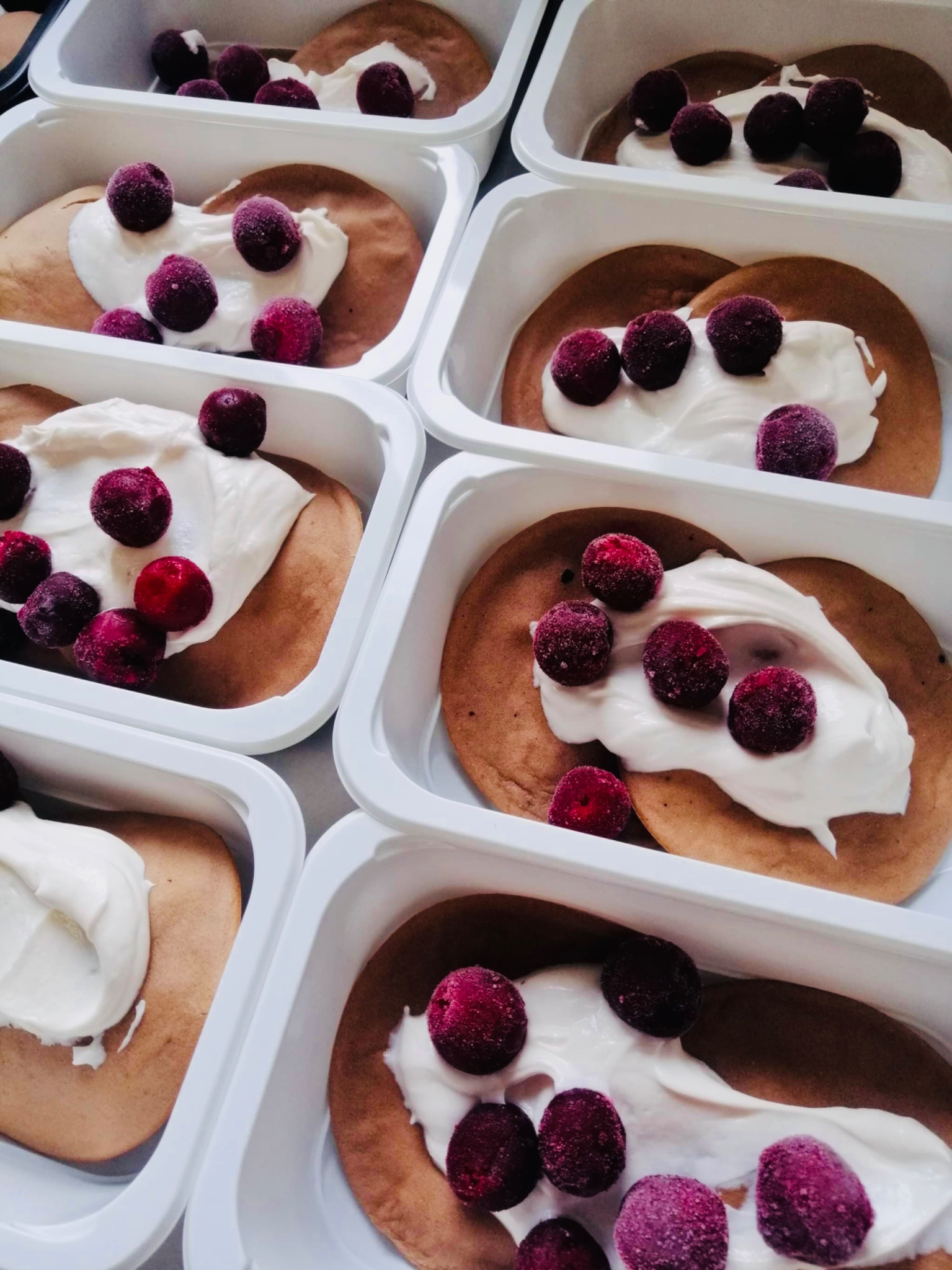 Pudełka z naleśnikami, porcją białego kremu i mrożonymi wiśniami, przygotowane do transportu.