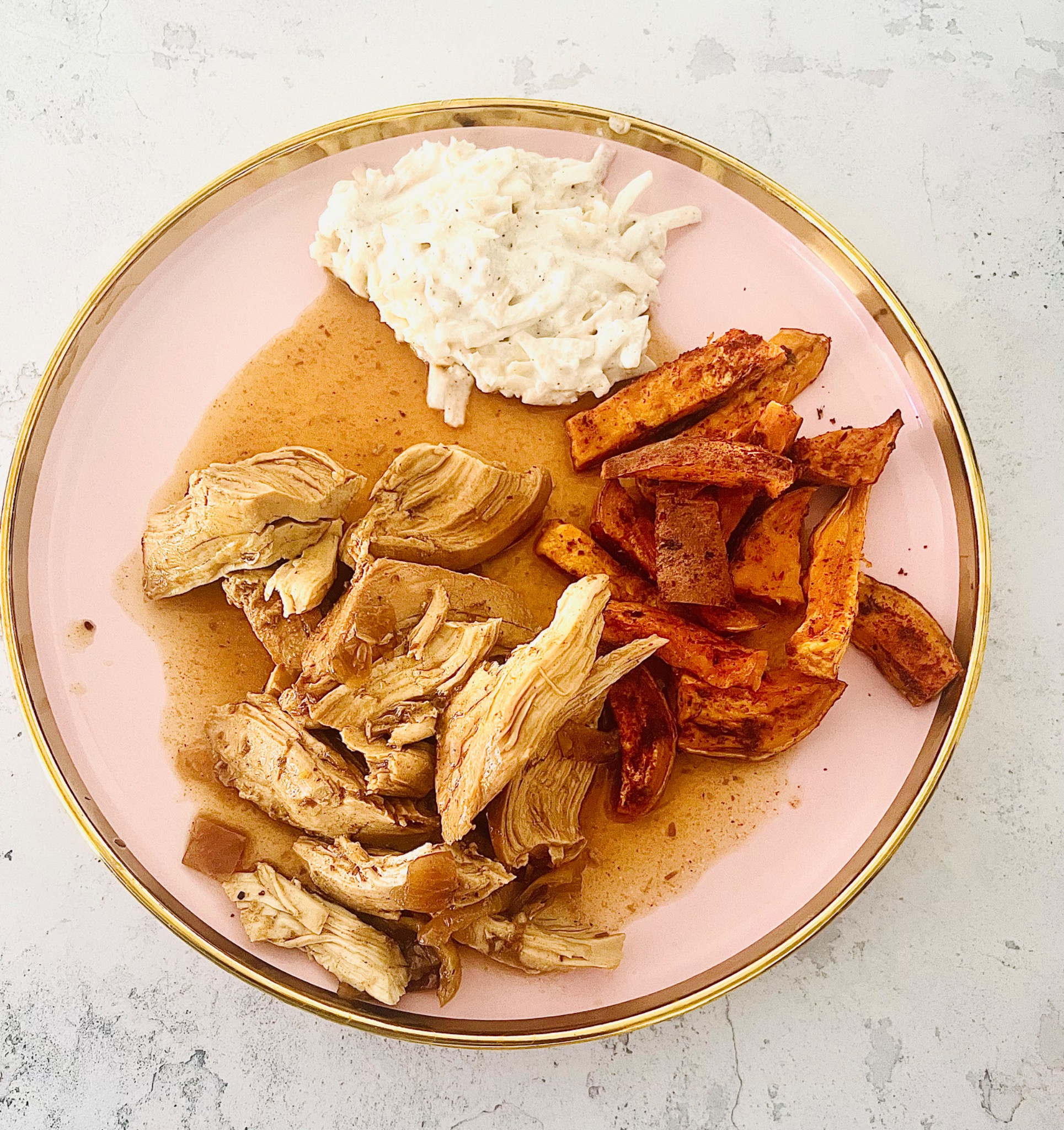 Danie na różowym talerzu ze złotym rantem: kawałki kurczaka w sosie, surówka z białej kapusty i pieczone bataty.