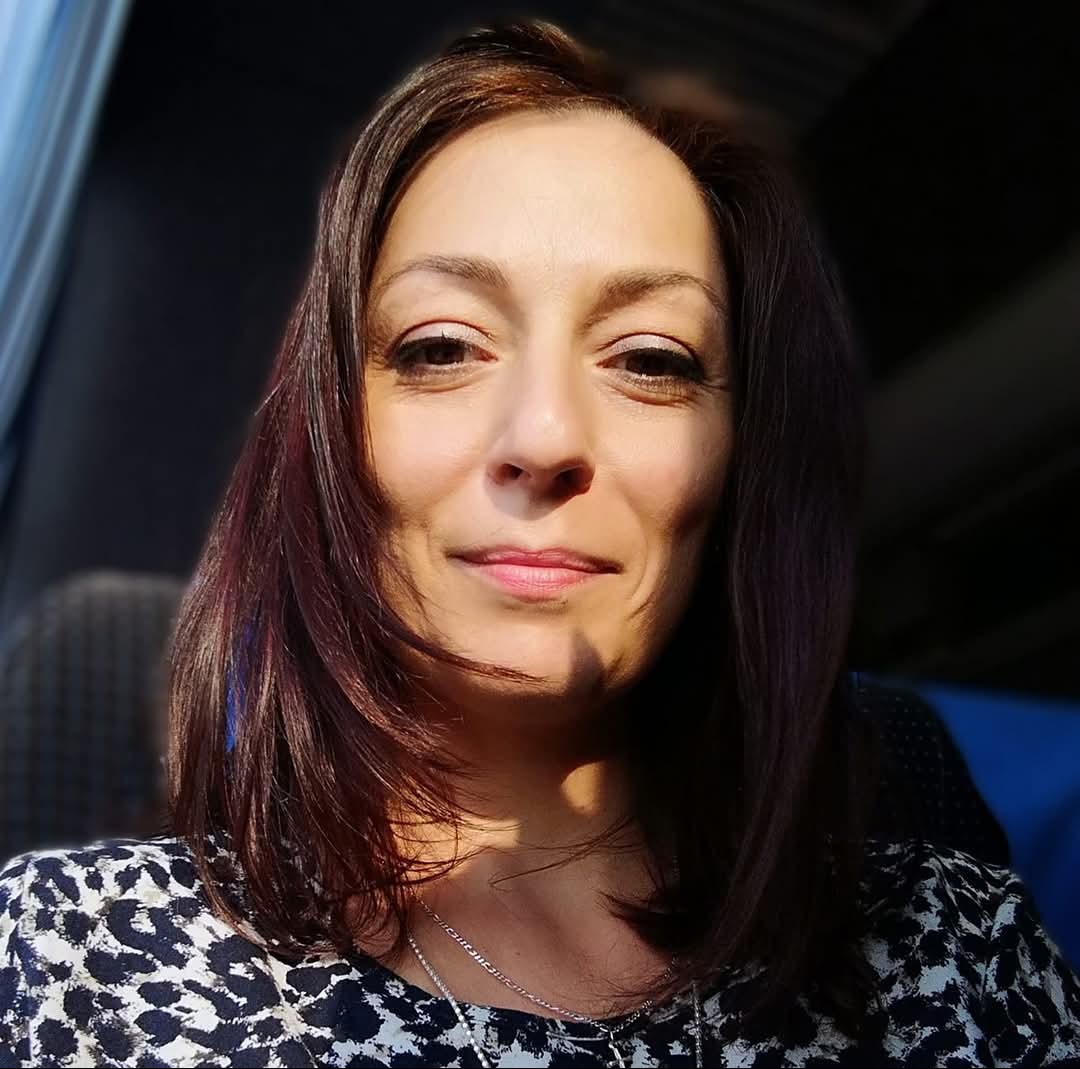 Portret uśmiechniętej kobiety z ciemnymi włosami w bluzce we wzory, oświetlonej bocznym światłem.