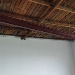 ZRKopytek - Czerwona belka stalowa zamontowana pod drewnianym sufitem, widoczna drabina oparta o ścianę, wnętrze w trakcie remontu.