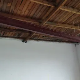 Czerwona belka stalowa zamontowana pod drewnianym sufitem, widoczna drabina oparta o ścianę, wnętrze w trakcie remontu.