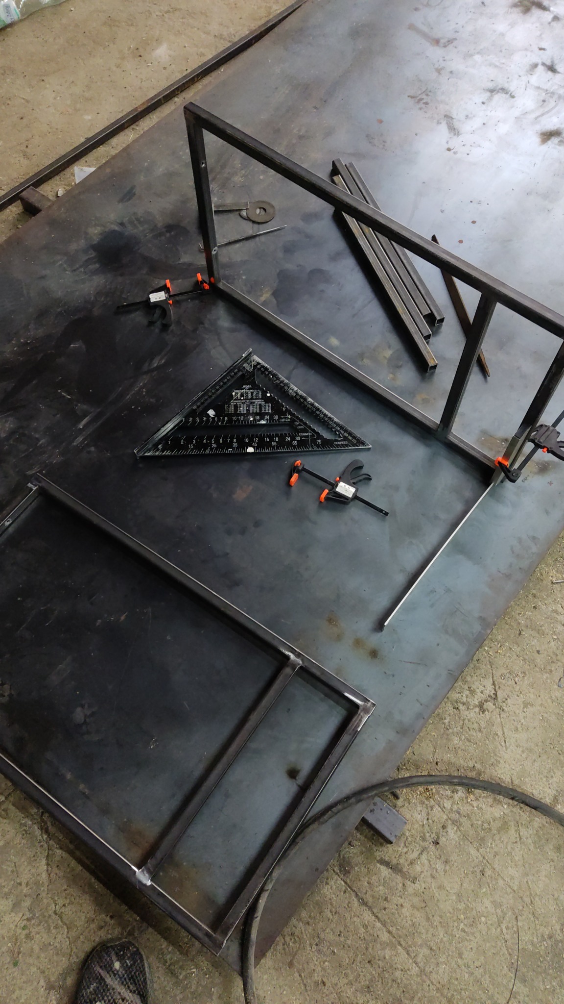 Spawanie metalowej konstrukcji w warsztacie w Rokicinach: fragment ramy, kątownik stolarski, ściski stolarskie i pręty na metalowym stole.