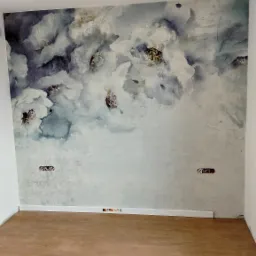 Ściana z dekoracyjną tapetą w kwiatowe wzory, widoczne gniazdka elektryczne i poziomica przy podłodze z paneli.