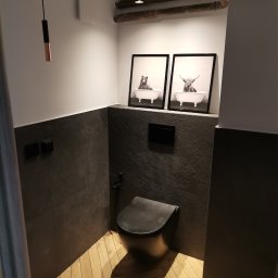 DOM ODNOWA DARIUSZ MARKIEWICZ - Nowoczesna toaleta w łazience z szarymi płytkami imitującymi kamień, drewnianą podłogą ułożoną w jodełkę i czarną wiszącą miską WC. Na ścianie wiszą czarno-białe grafiki zwierząt w wannie. Widoczne...