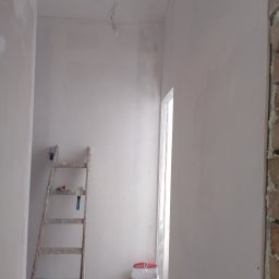 Artur Biernacki - Wnętrze w trakcie gładziowania ścian w Poznaniu, widoczna drabina malarska z narzędziami, wiadro z gładzią i surowy stan wykończenia podłogi.