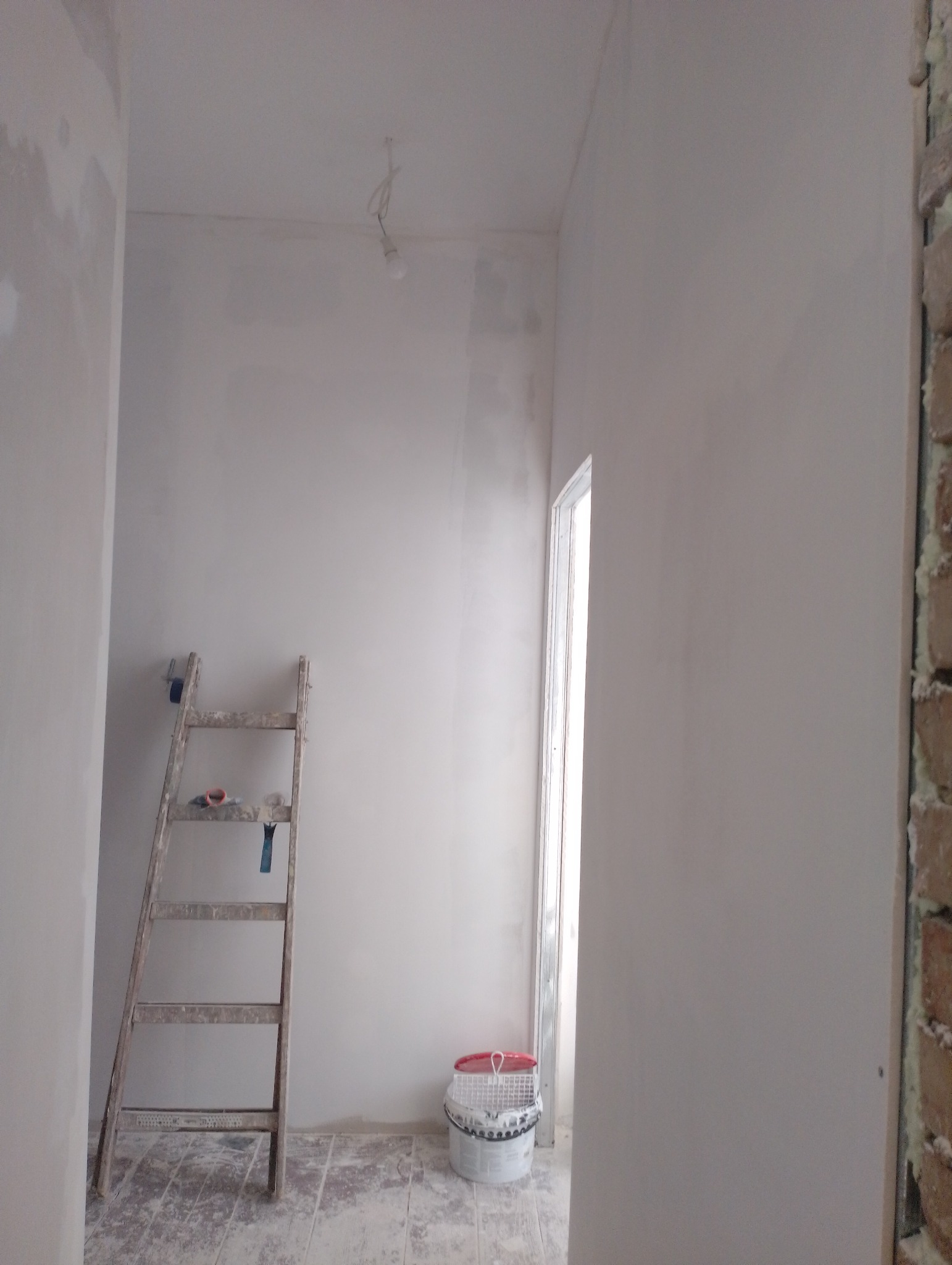 Wnętrze w trakcie gładziowania ścian w Poznaniu, widoczna drabina malarska z narzędziami, wiadro z gładzią i surowy stan wykończenia podłogi.