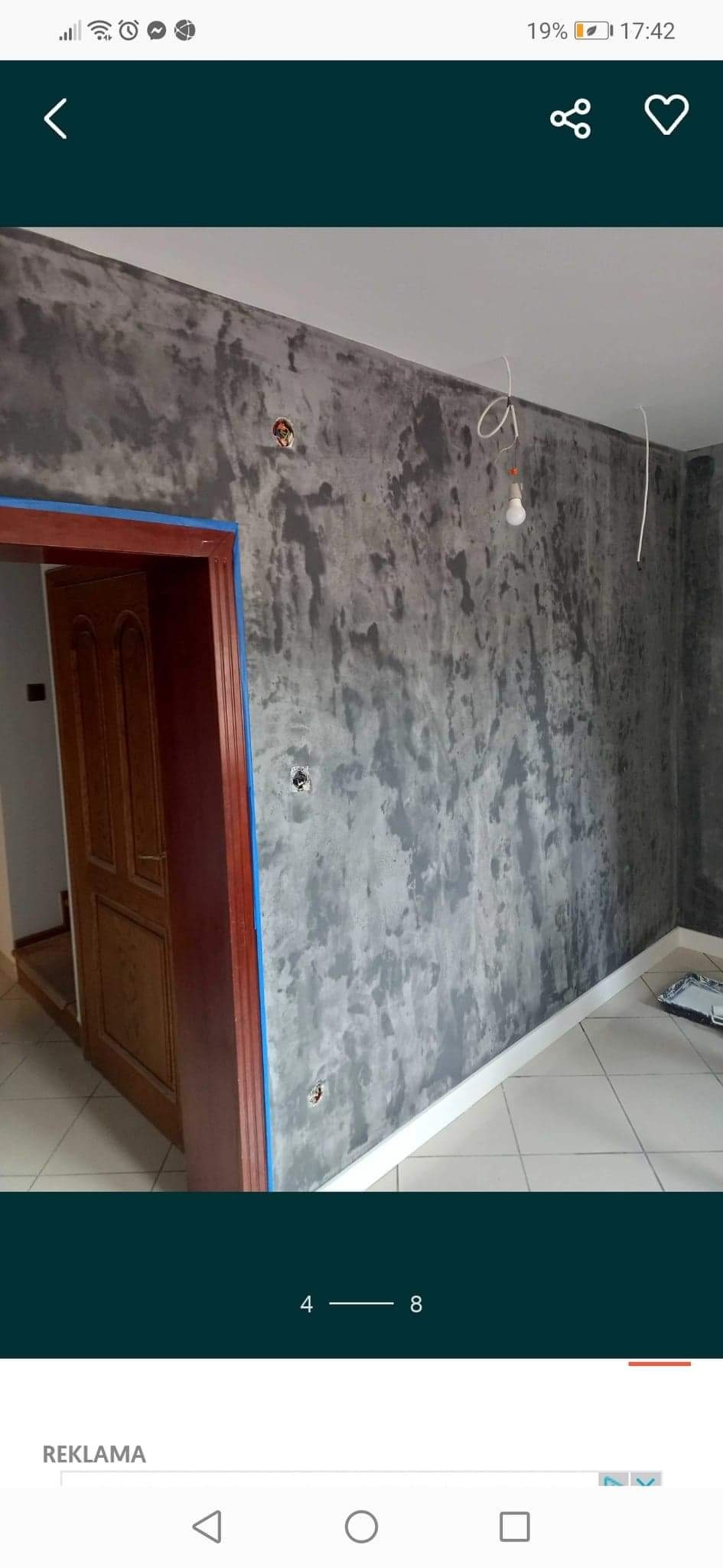 Ściana w pokoju po nałożeniu dekoracyjnej szarej gładzi, widoczne puszki elektryczne i kabel zwisający z sufitu, framuga drzwi zabezpieczona niebieską taśmą malarską.