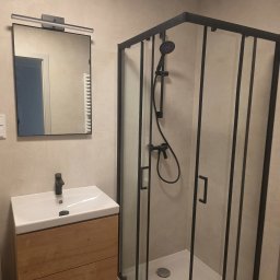 Remonty Volodymyr Muzyka - Nowoczesna łazienka z kabiną prysznicową w czarnej ramie, umywalką z drewnianą szafką i lustrem z oświetleniem. Beżowe płytki na ścianach tworzą spójną całość.