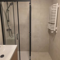 Remonty Volodymyr Muzyka - Nowoczesna łazienka z kabiną prysznicową typu walk-in z czarnymi profilami, grzejnikiem drabinkowym i umywalką nablatową na drewnianej szafce. Minimalistyczny design.