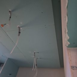 Remonty Volodymyr Muzyka - Zamontowana płyta karton-gips na suficie z wystającymi przewodami elektrycznymi, widoczne łączenia płyt i szpachlowane narożniki. Etap prac wykończeniowych.