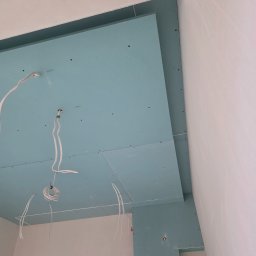 Remonty Volodymyr Muzyka - Niebieskie płyty kartonowo-gipsowe na suficie, widoczne kable elektryczne. Etap prac wykończeniowych w pomieszczeniu z surowymi ścianami.