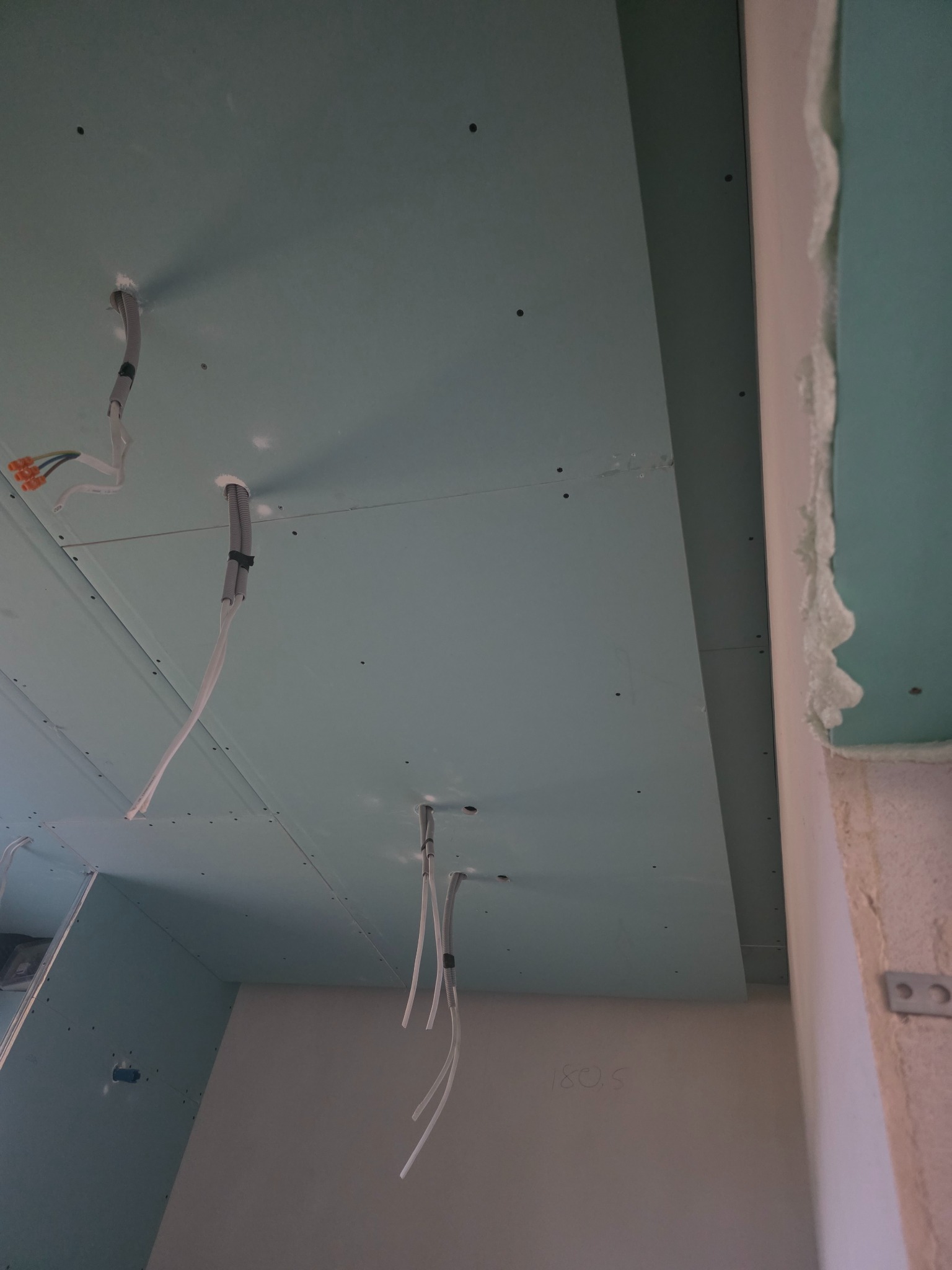 Zamontowana płyta karton-gips na suficie z wystającymi przewodami elektrycznymi, widoczne łączenia płyt i szpachlowane narożniki. Etap prac wykończeniowych.